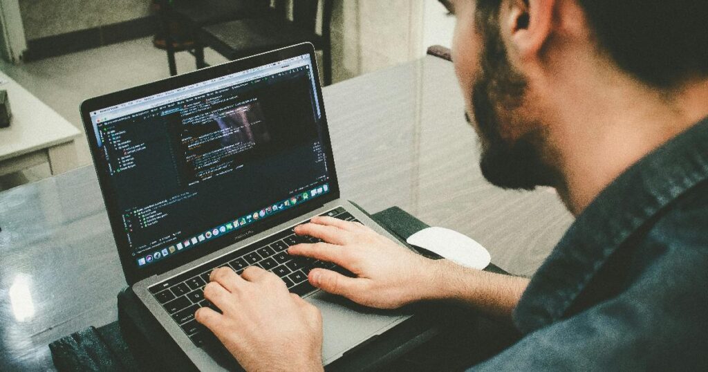 Two developers reviewing AI pair programming output from Codex and Claude Code on a laptop screen